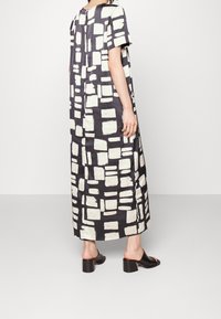 Vestido de patrón en blanco y negro con un corte holgado, mangas cortas y una silueta recta, combinado con sandalias con tacón grueso y deslizables.