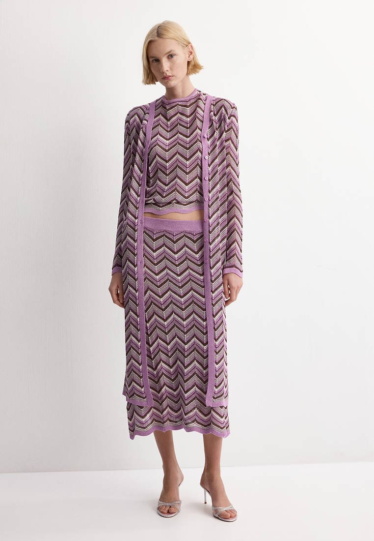 Femme portant une jupe en maille chevron violet, marron et blanc, un haut à manches longues assorti et un long cardigan ouvert devant avec des sandales à talons hauts.