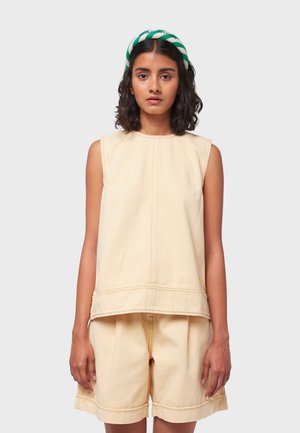 Beige sleeveless top and shorts made of soft fabric; shorts feature cuffed hems. Model wears a green and white striped headband.