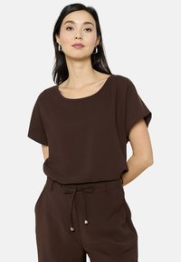 Top marrone a maniche corte realizzato in tessuto leggero, con scollatura rotonda e vestibilità comoda, abbinato a pantaloni con cordoncino coordinati.