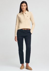 Polo de manga larga en beige con cuello y tapeta de botones. Pantalones azul marino oscuro y mocasines color cuero completan el conjunto. Diseño sencillo y entallado.