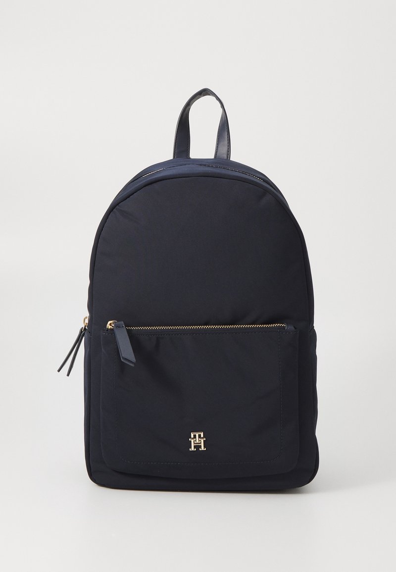 Mochila de nylon azul marino con una parte superior redondeada, herrajes dorados, un bolsillo frontal con cremallera y un acento de logo. Cuenta con un asa superior para llevar.