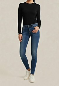 Jeans ajustados azul claro con cintura alta, confeccionados en denim. Combinados con una camiseta negra de manga larga y zapatillas blancas, mostrando una silueta entallada.