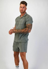 Kortärmad polo och shortsset i mjukt, texturerat grönt tyg. Funktioner en bröstficka och diskret varumärke på båda delarna.