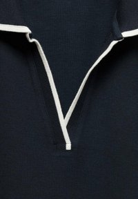 Marineblå polo-shirt med en kontrasterende hvid krave og knapstolpe. Blødt, tekstureret stof med et klassisk V-hals design.