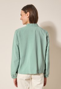 Veste légère de couleur vert menthe avec un col froncé et des poignets élastiques, offrant une coupe décontractée et une texture douce. Vue arrière affichée.