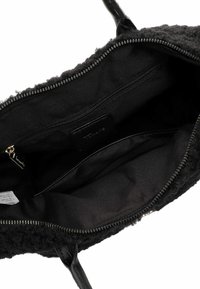 Borsa nera con un'esterno testurizzato e morbido. L'interno foderato presenta una tasca con zip e una sezione aperta con un'etichetta in pelle.