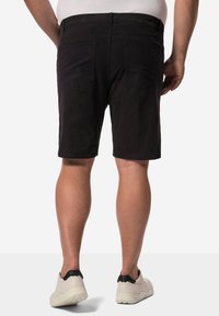 Pantalones cortos negros de corte recto, hechos de una tela suave. Incluyen bolsillos traseros y una cinturilla, combinados con zapatillas de color claro.