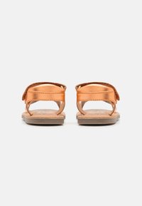 Sandali tan con cinturini in rame metallico, caratterizzati da un retro aperto e un design minimale. Sottopiede marrone con un leggero motivo di battistrada; suola piatta.