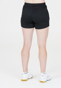 Svarta sportshorts med resårmidja, tillsammans med vita sneakers som har en texturerad sula och är ankellånga.