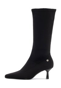 Bota negra hasta el tobillo hecha de un tejido elástico con punta afilada, tacón delgado y un acento de logo plateado en el lateral. Textura suave.
