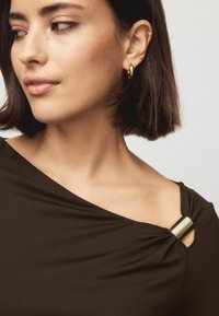 Brown fabric top featuring a gathered design with a gold accent at the shoulder, and a smooth texture. Simple and modern shape.