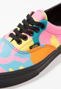 Gros plan sur une basket Vans multicolore avec des lacets noirs, présentant des motifs abstraits roses, bleus, jaunes, orange et verts, ainsi qu'une semelle noire.