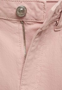 Lichtroze stof met een gladde textuur, voorzien van een zilveren rits en drukknoopsluiting. Inclusief stiksels langs de randen.