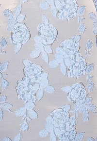 Tela de color gris claro con un patrón floral en relieve en suaves tonos de azul y acentos plateados, que presenta rosas y hojas a lo largo del diseño.