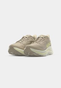 Beige running shoes with mesh upper, textured design, and a thick white midsole. Features a reflective logo in light green on the side.