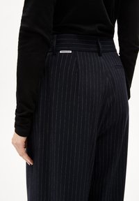 Marineblauwe pinstripe broek met plooien, met een gladde textuur, achterzak en een label op de tailleband. Contrasterende witte strepen.