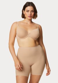 Reggiseno beige sagomato con spalline regolabili, realizzato in un tessuto morbido e con un gancetto centrale; abbinato a pantaloni corti beige a vita alta per un effetto levigante.