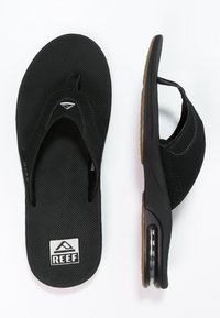 Fekete flip-flop papucsok, texturált gumitalppal, puha szövetpántokkal és enyhe sarkú párnázott talpbéléssel. A logo a talpon látható.