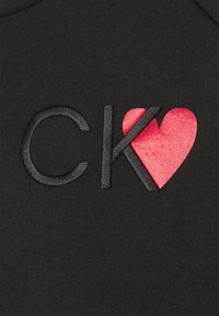 Tessuto nero con lettere ricamate "C K" in nero e un design di cuore rosso incorporato, che presenta una texture morbida e linee pulite.