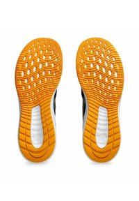 Schwarz-weiße Sportschuhe mit strukturierten orangen Außensohlen, die kreisförmige Ausschnitte und Wellenmuster aufweisen. Die Sohlen haben ein zulaufendes Design.