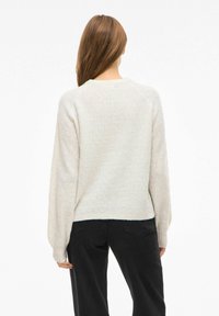 Gai bēšas krāsas džemperis ar teksturētu ģeometrisku rakstu, garām piedurknēm un noapaļotu kaklu; saskaņots ar melnām biksēm.