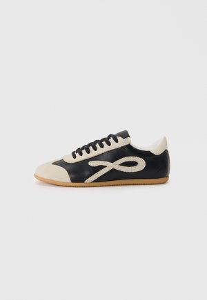 Sneaker in pelle nera e beige con punta arrotondata, design con lacci e un accento distintivo del logo. Suola in gomma offre una maggiore aderenza.