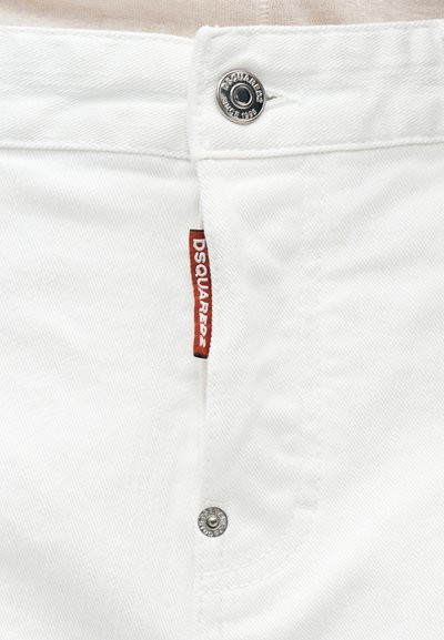 Κοντινή λήψη λευκών τζιν από denim με μεταλλικό κουμπί και κόκκινη ετικέτα DSQUARED2 στην περιοχή του φερμουάρ.