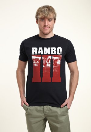 Sort bomulds T-shirt med stor hvid "RAMBO" tekst med røde accenter og en slidstærk grafik af figurer nedenunder, rund halsudskæring.