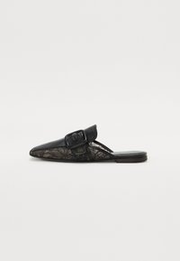 Mules en dentelle noire avec un bout pointu et un large détail de boucle noire. Elles présentent un talon plat et une combinaison de matériaux en cuir et en dentelle.