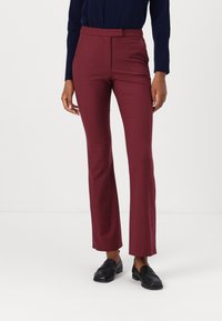 Pantalones acampanados burdeos hechos de una tela suave, con un frente plano y una cinturilla con cierre de gancho. Combinados con mocasines negros.