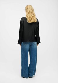 Schwarze Satin-Bluse mit langen Ärmeln, kombiniert mit weiten blauen Denim-Jeans. Die Jeans haben eine hohe Taille und Gesäßtaschen, was einen lässigen Look unterstreicht.
