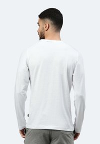 Weißes Langarm-T-Shirt aus Baumwolle mit rundem Halsausschnitt und glatter Textur, mit dezentem Nähen und seitlichen Etiketten.