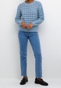 Lichtblauwe gebreide trui met een gestructureerd patroon, ronde hals en lange mouwen, gecombineerd met lichtblauwe jeans en zwarte instappers.