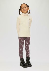 Crème coltrui met een zilveren sterdetail, gecombineerd met bordeaux leggings met witte eenhoorn- en sterpatronen, aangevuld met zwarte laarzen.