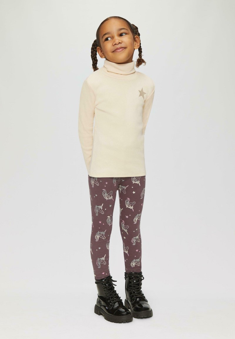 Crème coltrui met een zilveren sterdetail, gecombineerd met bordeaux leggings met witte eenhoorn- en sterpatronen, aangevuld met zwarte laarzen.