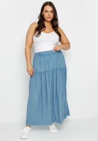 Ljusblå maxikjol i mjukt material med tierad design, försedd med elastisk midja och avslappnade vita sneakers.