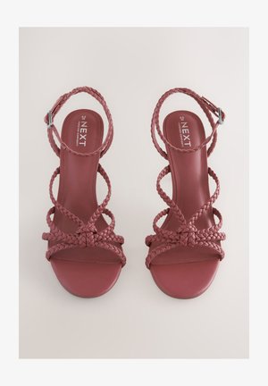 Rote geflochtene Sandalen mit Absatz, offenem Zehenbereich und Knöchelriemen, mit glatter matter Sohle und ineinander verflochtenen Riemen für Halt.