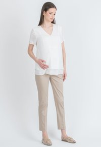Bílá blůza s krátkým rukávem a výstřihem do V, s vrstveným lemem, spárovaná s béžovými, slim-fit kalhotami. Doplňky zahrnují vzorované baleríny.