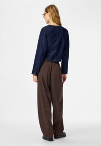 Veste en denim courte à manches longues, associée à un pantalon large rayé marron. La tenue présente une coupe décontractée et un design minimaliste.