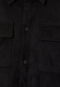 Chemise noire à texture douce avec deux poches poitrine à rabat et boutons-pression noirs mats sur le devant.