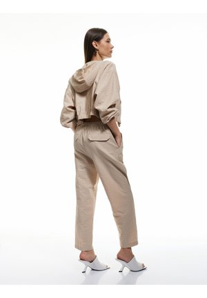 Sudadera corta de color beige y ligera con cordón, combinada con pantalones holgados con bolsillos. Mules de tacón abierto blancos.