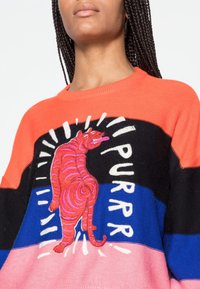 Kleurrijke trui met een gestreept patroon in oranje, zwart, blauw en roze. Opvallende geborduurde roze tijgerafbeelding met de tekst "PURRR".