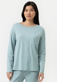 Haut à manches longues bleu clair en tissu doux, avec un col rond et une poche poitrine. Les manches sont ajustées aux poignets.