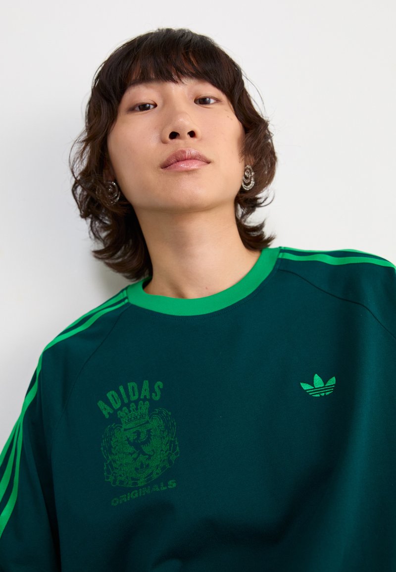 Groene en marineblauwe oversized sweatshirt met een bedrukte logo en ontwerp, contrasterende groene strepen op de mouwen en een ronde halslijn.