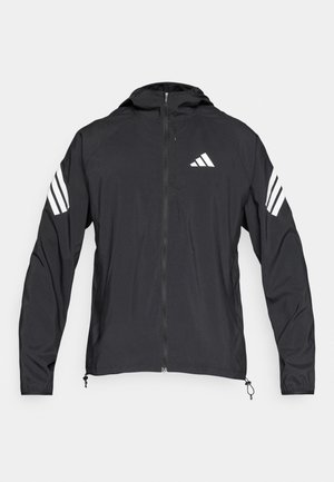 Giacca a vento nera con zip frontale, cappuccio e dettagli a tre strisce bianche sulle maniche. Realizzata in tessuto leggero e liscio.