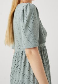 Helles blaues Kleid mit kurzen Puffärmeln, das ein Chevron-Muster aus Lochstickerei und eine geraffte Taille aufweist.