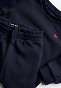 Marineblaue Sweatshirt und passende Jogginghosen aus weicher Baumwolle. Das Sweatshirt hat gerippte Bündchen und ein gesticktes rotes Logo. Die Hose verfügt über einen elastischen Bund.