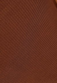Un tissu marron à côtes avec une texture douce, comportant des lignes verticales. Le matériau semble élastique et étroitement tissé.