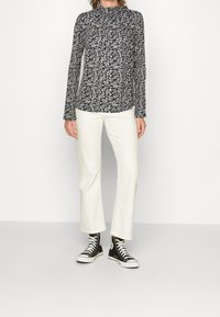 Bloemachtige blouse met lange mouwen in marineblauw met een hoge halslijn, gecombineerd met witte flared broek en zwarte hoogtop sneakers.